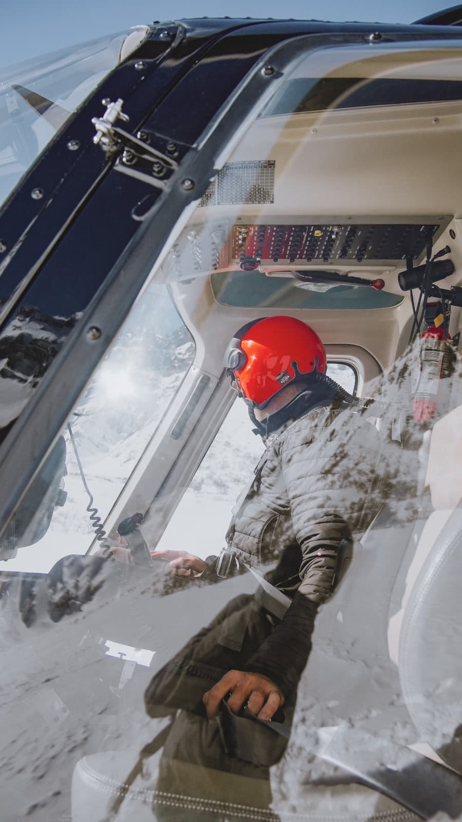 Private heli-skiing pilot inside the cockpit with mountain reflections on the glass